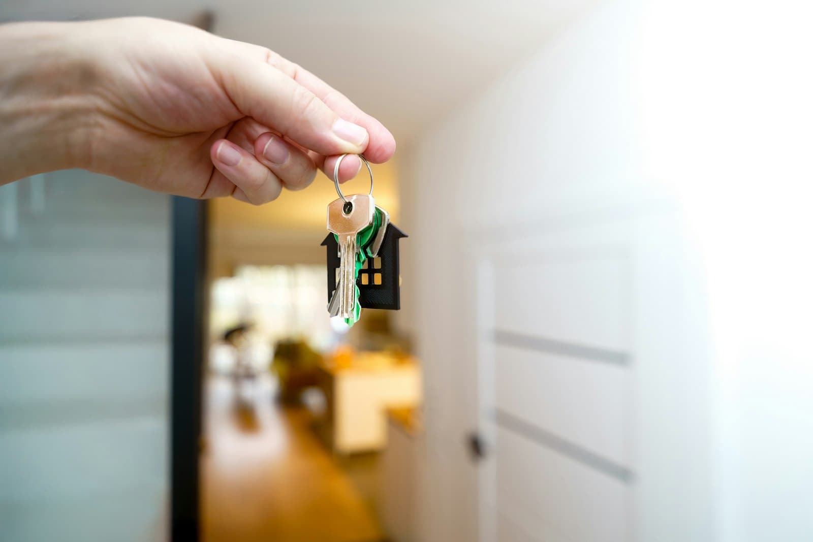 A hand holding house keys in front of a home's entry